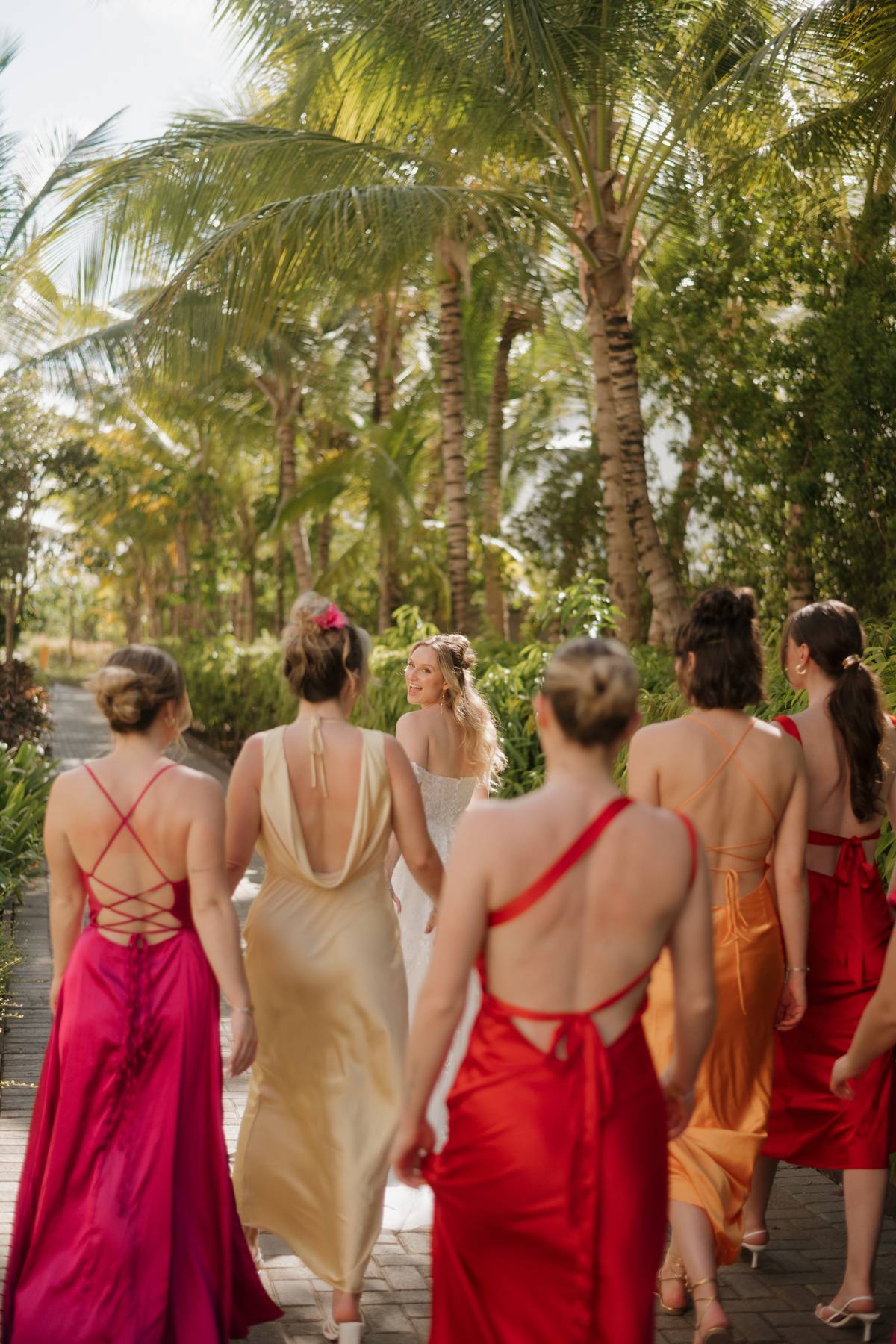 Group of women in colorful dresses walking through a tropical setting with palm trees.