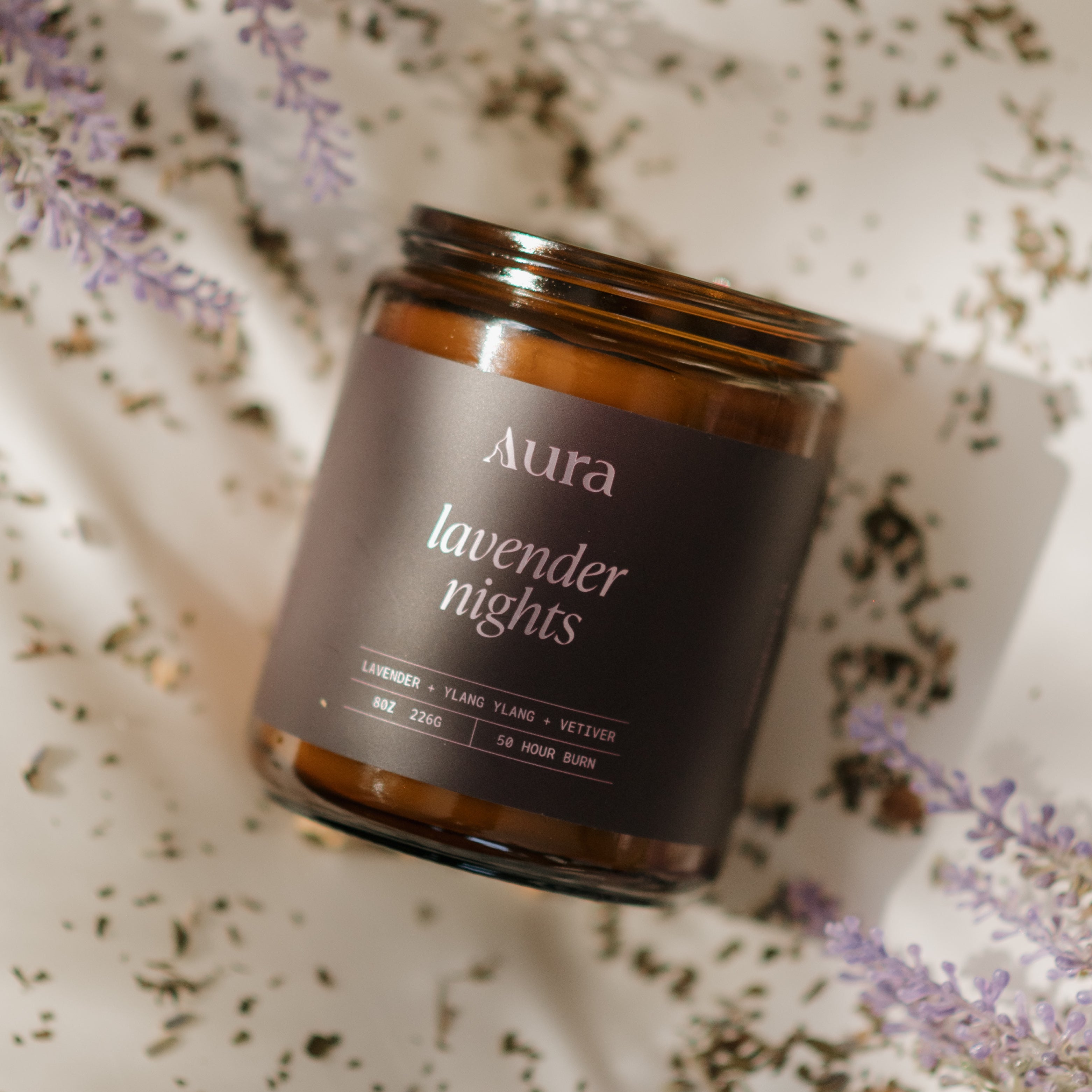 Aroma candle labeled 'Aura Lavender Nights' on a textured surface with lavender flowers.